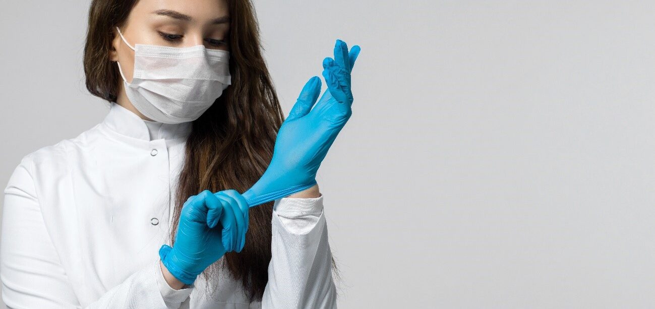 Young doctor, dark-haired and light-skinned pants blue surgical gloves. She&apos;s wearing a mask. prepared to face covid-19